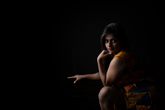 Fashion portrait of an young and attractive Indian Bengali brunette girl with colorful western dress in front of a black studio copy space background. Indian fashion portrait and lifestyle.