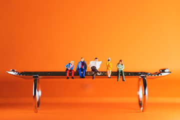 Miniature people, man and woman sitting on steel bench using as business and social concept