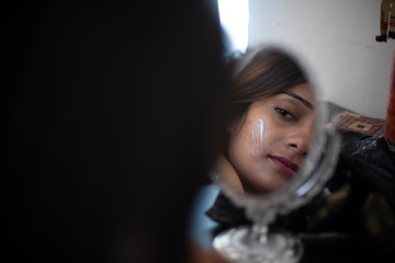 Reflection of an young and attractive Indian Bengali brunette woman is looking her face in a mirror while tying her hair in the morning in her room. Indian lifestyle.