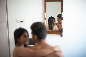 Semi nude couple wrapping with a blanket while sitting on the bed with the upper half of their body exposed in an intimate mood in a winter morning. Indian lifestyle and intimate couple.