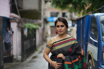 Portrait of a beautiful brunette Indian bengali thoughtful woman in traditional wear sari standing...