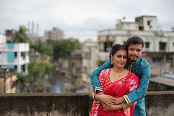 Fototapeta premium A brunette Indian Bengali romantic couple in traditional wear interacting between themselves on a roof top in romantic mood in the morning of Durga Puja festival in urban background. Indian lifestyle.