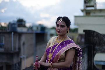 Portrait of a beautiful smiling brunette Indian Bengali bride in traditional sari standing on the roof top in afternoon under blue sky. Indian lifestyle.