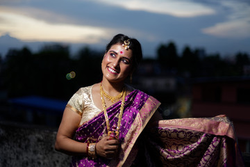 Fototapeta na wymiar Portrait of a beautiful smiling brunette Indian Bengali bride in traditional sari standing on the roof top in evening. Indian lifestyle.