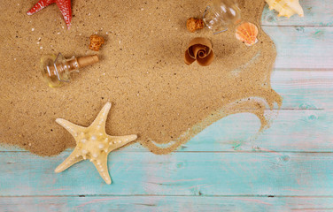 Starfish with seashells on sand on blue wooden background. Papyrus from the glass bottle with cork.