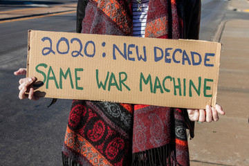 Protest War 2020-New Decade-Same War Machine - woman in scarf holds homemade sign