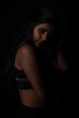 Fashion portrait of an Indian brunette Bengali dark skinned woman with black lingerie standing in black studio copy space background. Indian fashion photography and lifestyle.