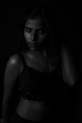 Monochrome fashion portrait of an Indian brunette Bengali dark skinned woman with black lingerie standing in black studio copy space background. Indian fashion photography and lifestyle.