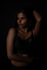 Obraz na płótnie Canvas Fashion portrait of an Indian brunette Bengali dark skinned woman with black lingerie standing in black studio copy space background. Indian fashion photography and lifestyle.