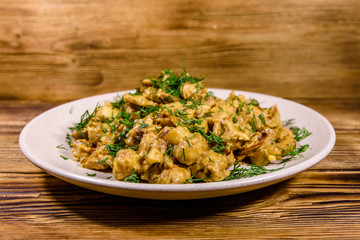Plate with champignons stewed in sour cream on a wooden table
