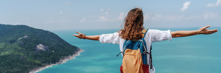 Girl relaxing on tropical hill top with arms open felling freedom witn beautiful ocean view from top. Freedom and happiness concept.