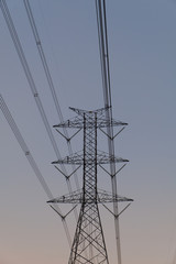 A picture of a high-voltage electricity pole made of steel, with many wires passing across in the evening sky background.