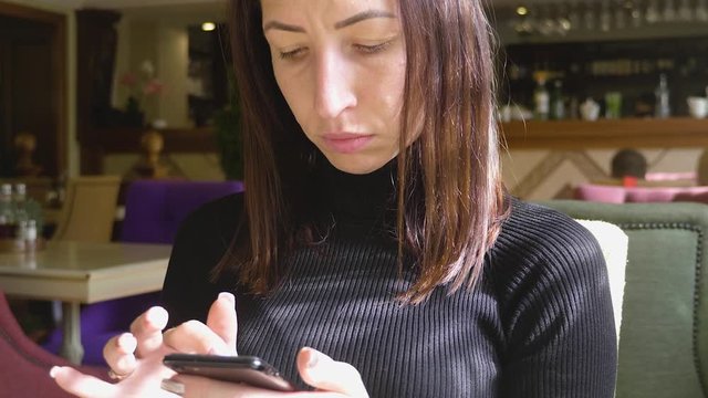 Young wonam use mobile phone while sitting in comfortable coffee shop during work break, charming happy female reading fashion news on cell telephone during breakfast in restaurant.