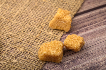 Bits of brown sugar and coarse homespun cloth on a wooden background. Close up.