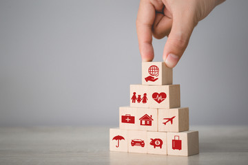 Hand arranging wood block stacking with icon insurance: car,  real estate and property, travel, finances, health, family and life, insurance concept.