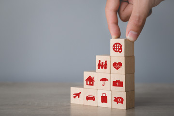 Hand arranging wood block stacking with icon insurance: car,  real estate and property, travel, finances, health, family and life, insurance concept.
