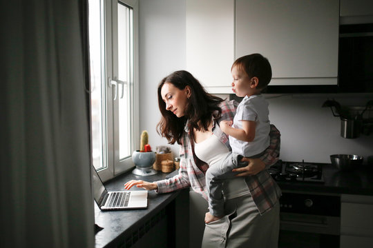Busy cute woman mom holding baby works on laptop