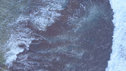 Above the ocean, aerial lock down view at foaming waves and surface near coast line