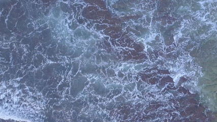 Fototapeta na wymiar Above the ocean, aerial lock down view at foaming waves and surface near coast line