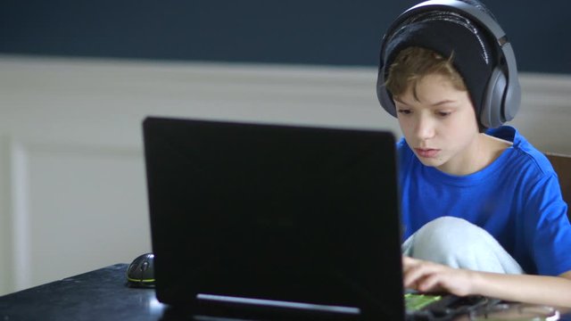 Young boy playing on his laptop and wearing headphones
