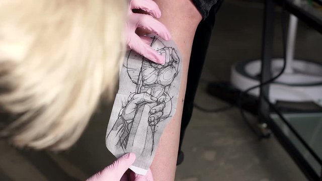 Tattoo artist puts a picture on a young woman's leg, the process of creating a tattoo. Man doing picture on a leg of man. Tattooist makes a tattoo. Close-up.