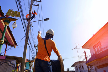 Focus on foreground and low angle view of electricians team are working to install electrical systems on electric power poles with flare light and blue sky background at morning time