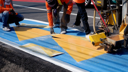 Road workers group in reflective vests with thermoplastic spray road marking machine are working to paint traffic lines and sign on asphalt road surface in the city, selective focus