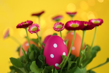 Easter holiday. Pink and  easter eggs in pink daisies colors on a bright yellow background with golden bokeh.Easter religious festive spring background.