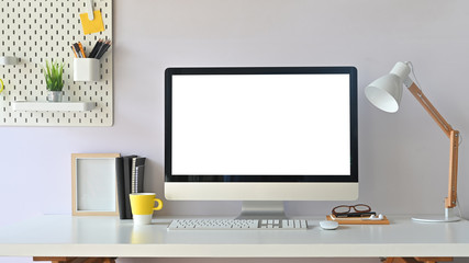 Workspace computer mockup and office supplies with peg board on wooden table.