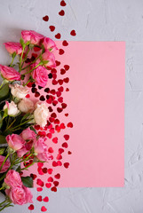 Valentine's Day background. Roses on pastel pink background  and a red confetti heart. Valentines day concept. Flat lay, top view, copy space.