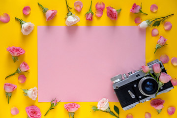 Round frame floral pattern  made of pink and beige roses, green leaves and film camera on yellow background.Valentine's Day background. Flat lay, top view.