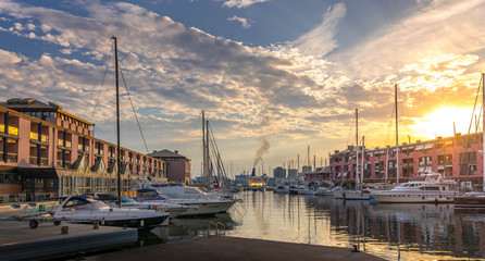 Genova, Genoa, Liguria, Italy: Beautiful sunset view of old harbor (Porto Antico), sailboats docked at quay nearby aquarium, reflections on water, sun setting