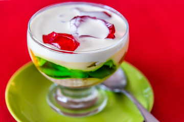 A serving of 'Trifle' in a clear desert bowl with green and red jelly, custard and whipped cream.