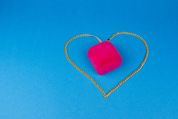 A chain of red gold in the shape of a heart and a pink box inside on a blue background.