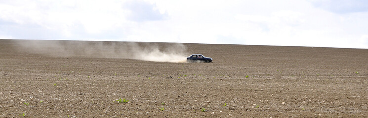 Obraz na płótnie Canvas The car goes quickly across the field. Clubs of dust ...