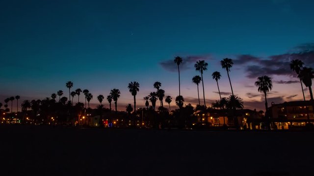 Time lapse in motion or hyper-lapse of sun setting over Santa Barbara beach in California with coastline and palm trees.