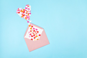 Pink envelope with heart shaped confetti over the blue background. Love, letter, message, saint valentines day concept. Flat lay, top view