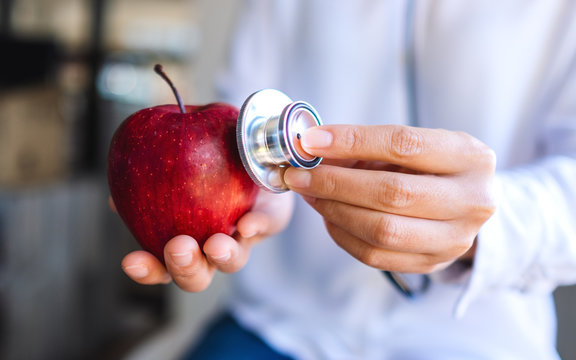 Closeup image of a doctor using stethoscope to examine a red apple
