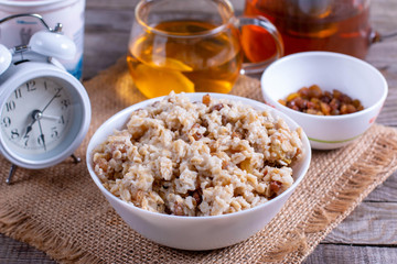 Delicious oatmeal porridge with raisins, butter and honey on a white plate on a wooden background