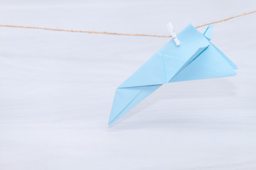 Fear of flying, plane crash or aerophobia concept. Blue paper plane upside down, plane hanging on a thread.