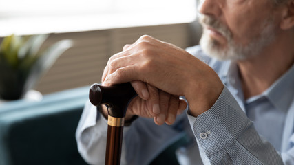 Elderly man sitting indoors closeup focus on hands holding cane