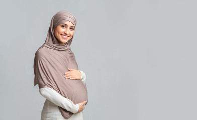 Portrait of beautiful pregnant muslim woman in hijab over gray background