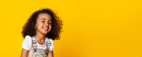 Cute little black girl sincerely laughing over yellow background, long panorama