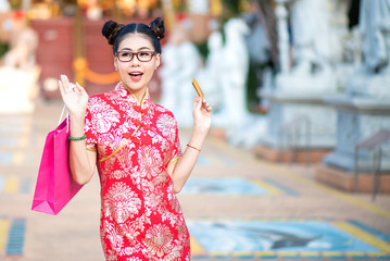 Shocked amazed Asian Chinese Woman in Cheongsam Traditional Red Dress Holding Shopping Bag and Paid Via Credit in Chinese Lunar New Year Festival