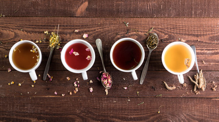 Assortment of cups of tea and dry tea in spoons on a wooden background. Top view with copy space.