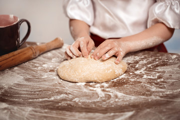 Hands of the child knead dough on a table. Soft focus.