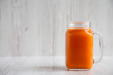 Homemade Mango Carrot Smoothie in a glass jar mug over white wooden background, side view. Copy space.