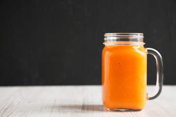 Homemade Mango Carrot Smoothie in a glass jar mug, side view. Space for text.