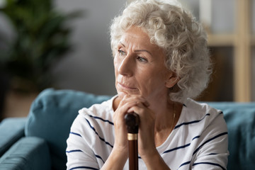 Fototapeta na wymiar Disabled mature woman sit on sofa holding cane looking away