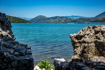 Fototapeta na wymiar Sunny spring day view of salt lagoon lake, valley and mountain in the national park of Butrint in Albania, Europe. Fortress stone ruined wall in the foreground.